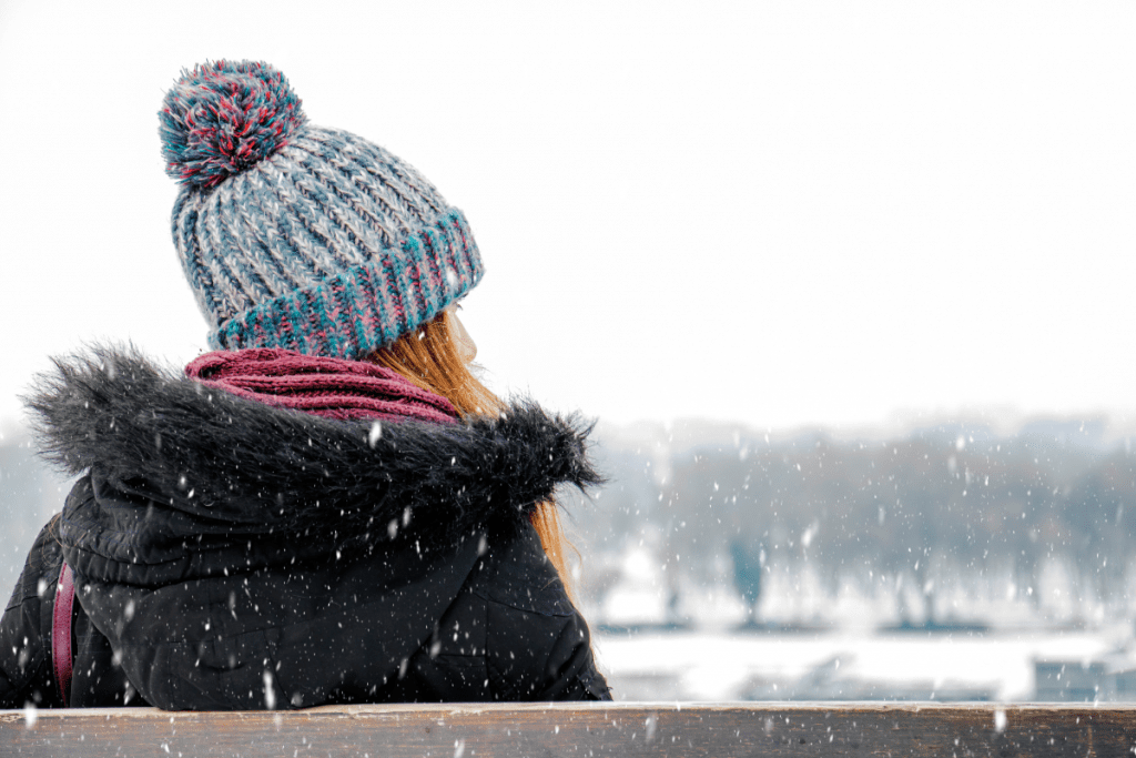 woman in hat and coat on bench in the snow