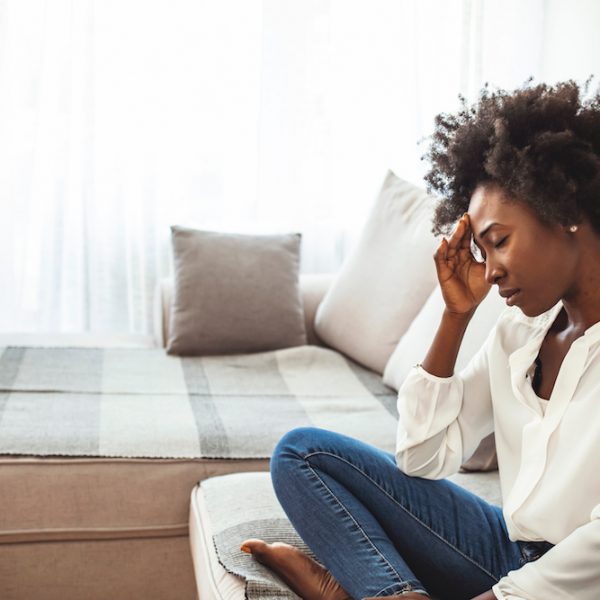 Close up african female sit on couch feels unhappy desperate thinking about personal difficulties mental health problems, 30s sad woman need psychological support goes through divorce break up concept